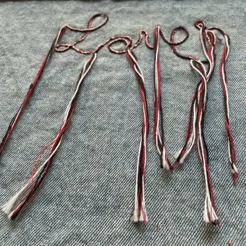 Custom computerized embroidery in denim with handwriting-style, three-color cord embroidery and long-fringe tassels